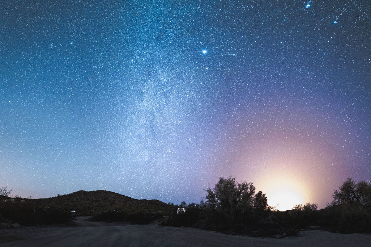 Night sky full of stars and a burst of orange light on the horizon