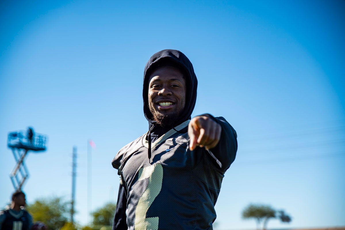 A football player points and smiles at the camera, blue sky in the background