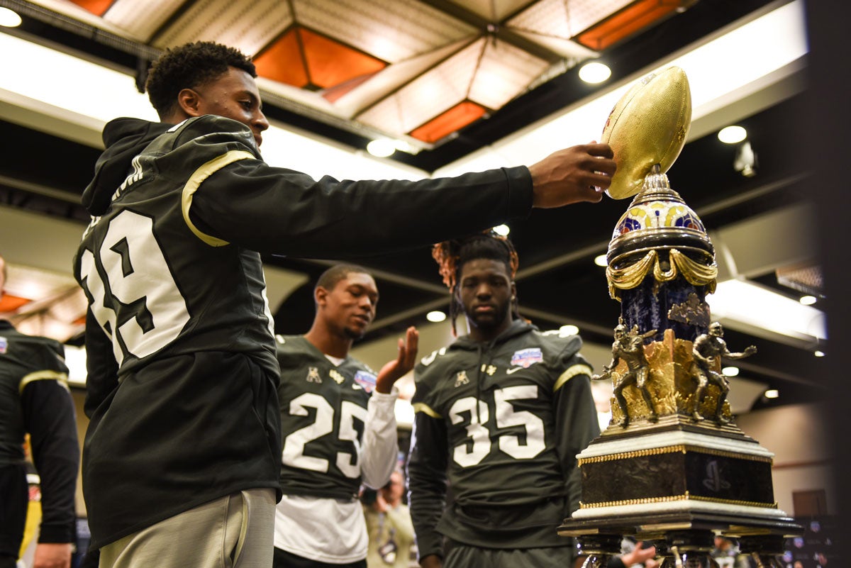 Three football players admire the Fiesta Bowl trophy
