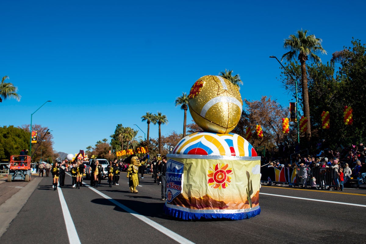 Parade float of a glitter football trophy as it makes it way down the street on a cloudless blue sky day.