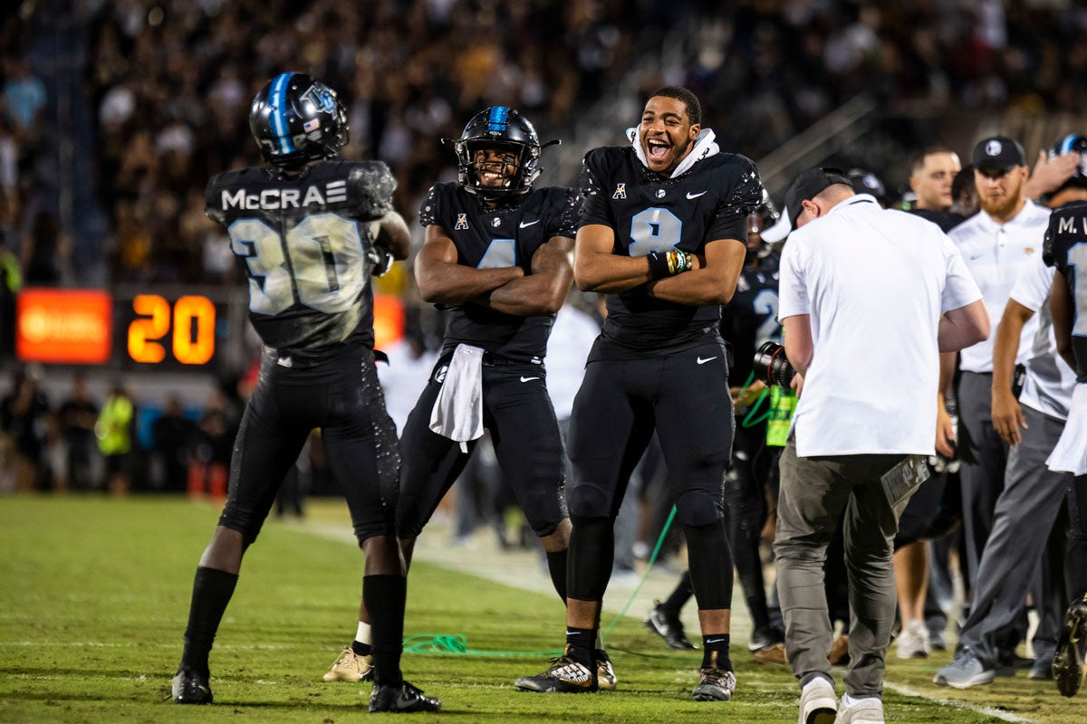 Three UCF players wearing black uniforms pose with arms crossed facing each other