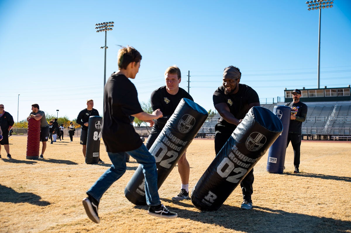 Two players hold tackling mats as a teenage boy rushes to tackle