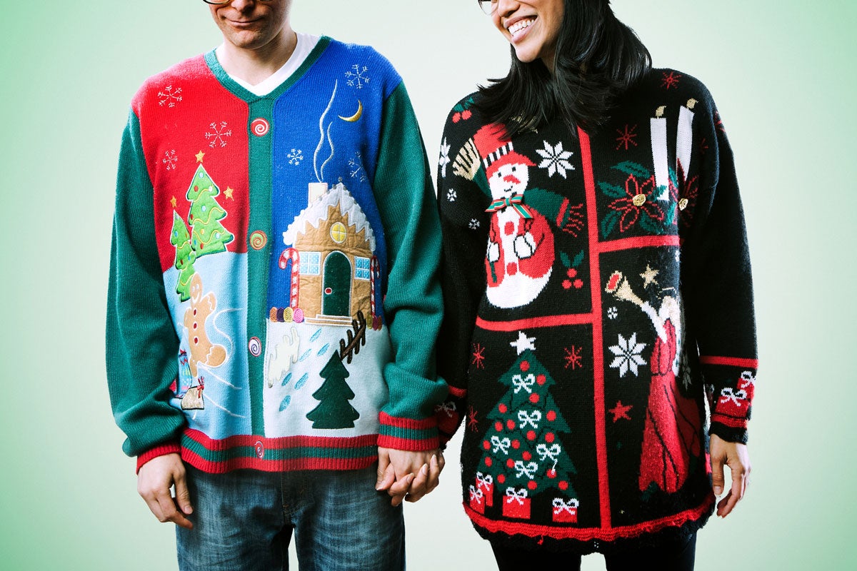 A man and a woman hold hands while wearing ugly holiday sweaters