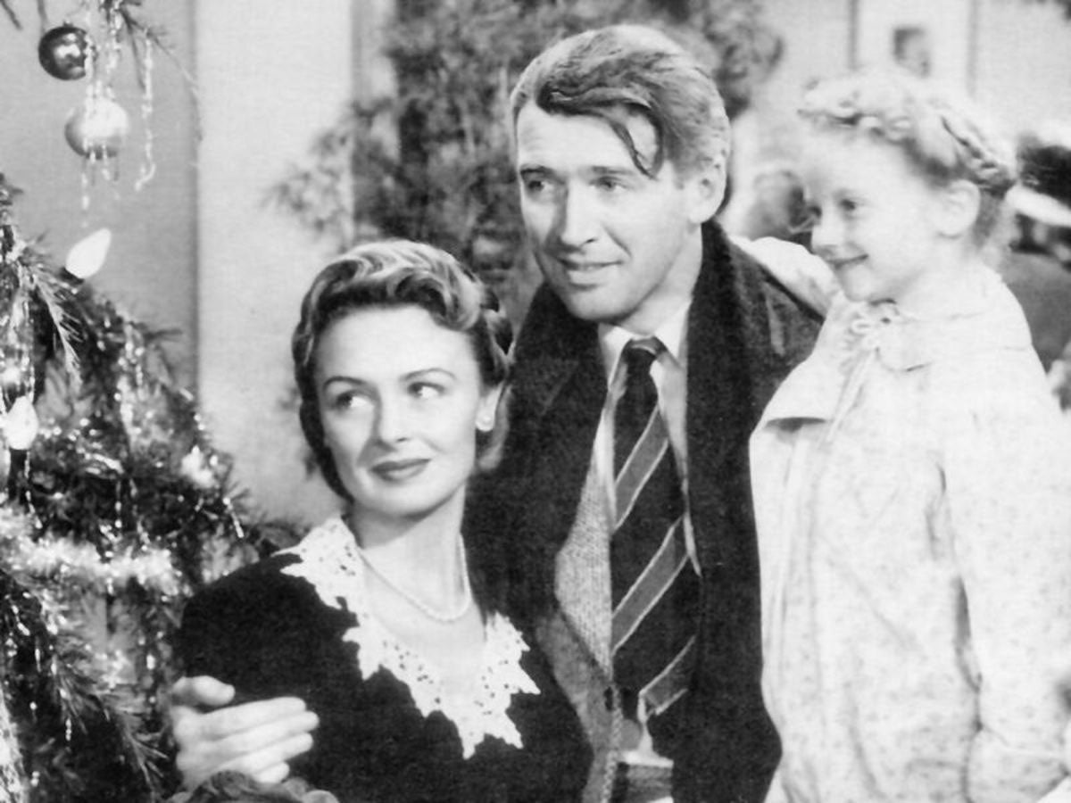 black and white photo of cast of It's A Wonderful Life, man wearing a jacket and tie hugs woman wearing a black and white top and a young girl wearing a white dress