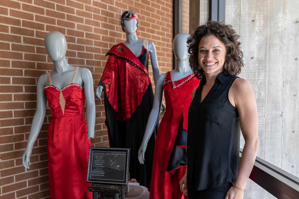 Brunette woman stands in front of three mannequins wearing red dresses