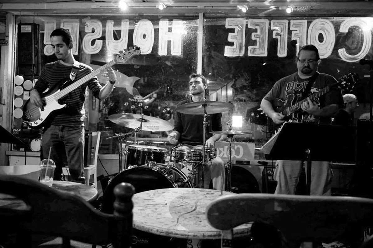 Three musicians stand and play instruments in front of Coffee House window