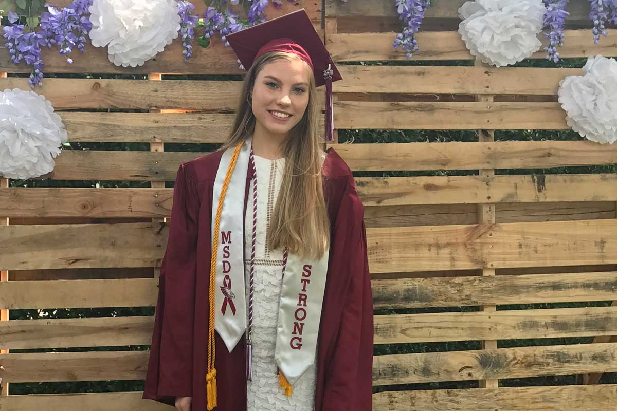 Blonde high school graduate wearing a red cap and gown