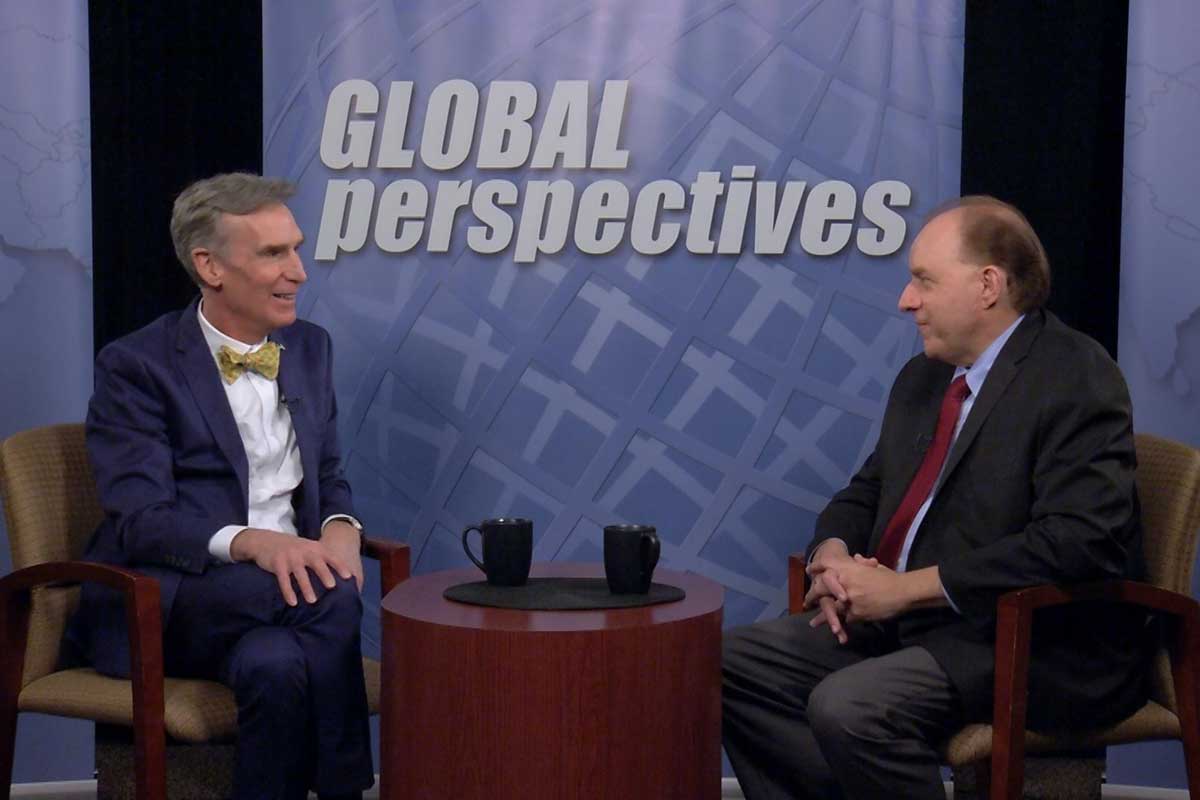 Two men sit at a table with a banner in the background that reads GLOBAL perspectives