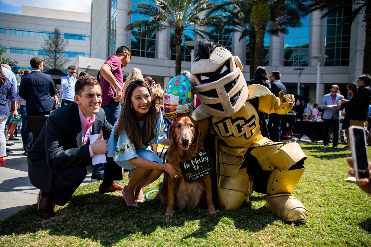 UCF mascot Knightro knees next to a man and woman and golden retriever