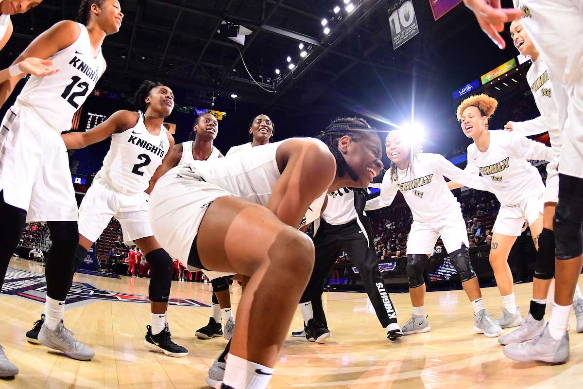 Women's basketball players huddle in a circle on court