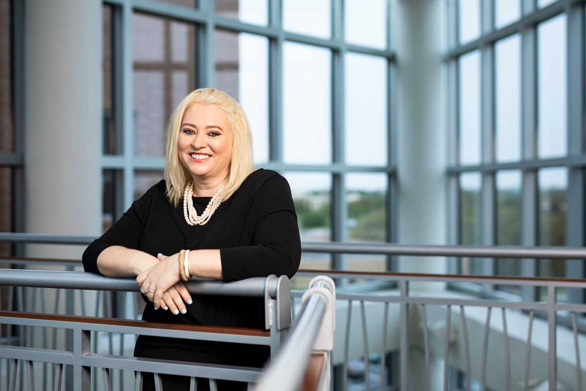 Blonde woman wearing black dress and white pearl necklace leans on stair railing