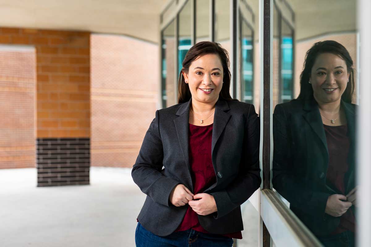 Woman wearing dark business jacket and maroon shirt leans against wall