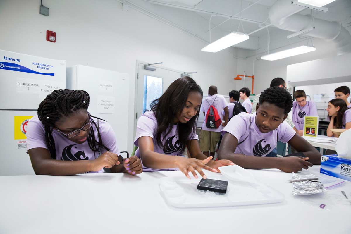 Three students in purple shirts sit at a white table