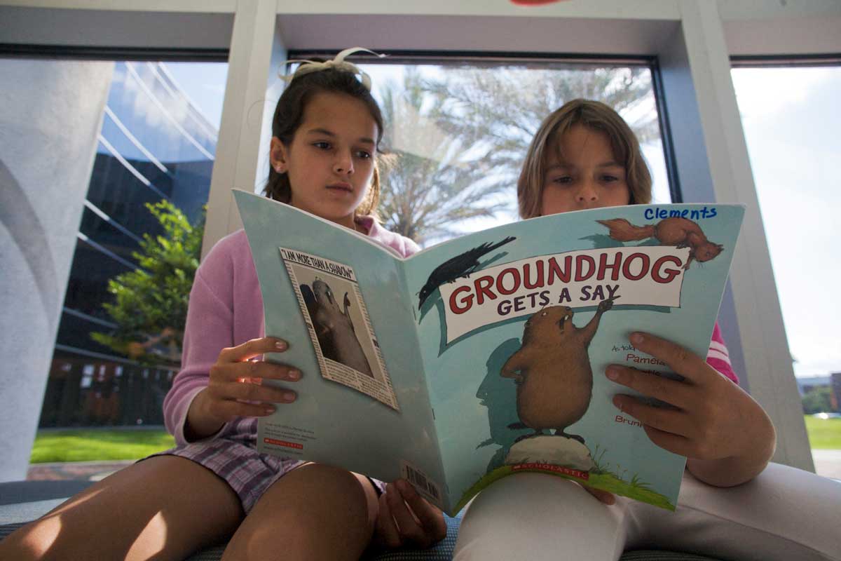 two children read "Groundhog Gets a Say" book in front of window