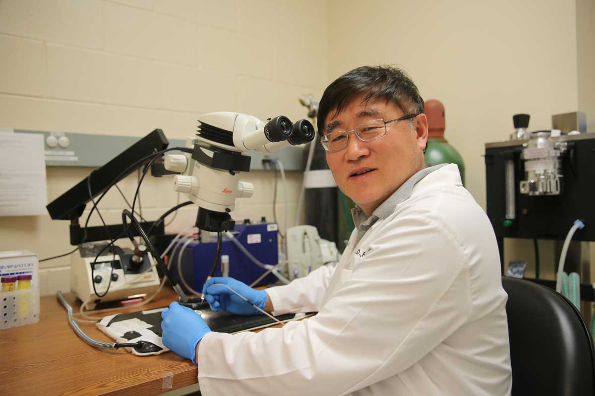 Man wearing white coat and blue medical gloves sits at lab bench