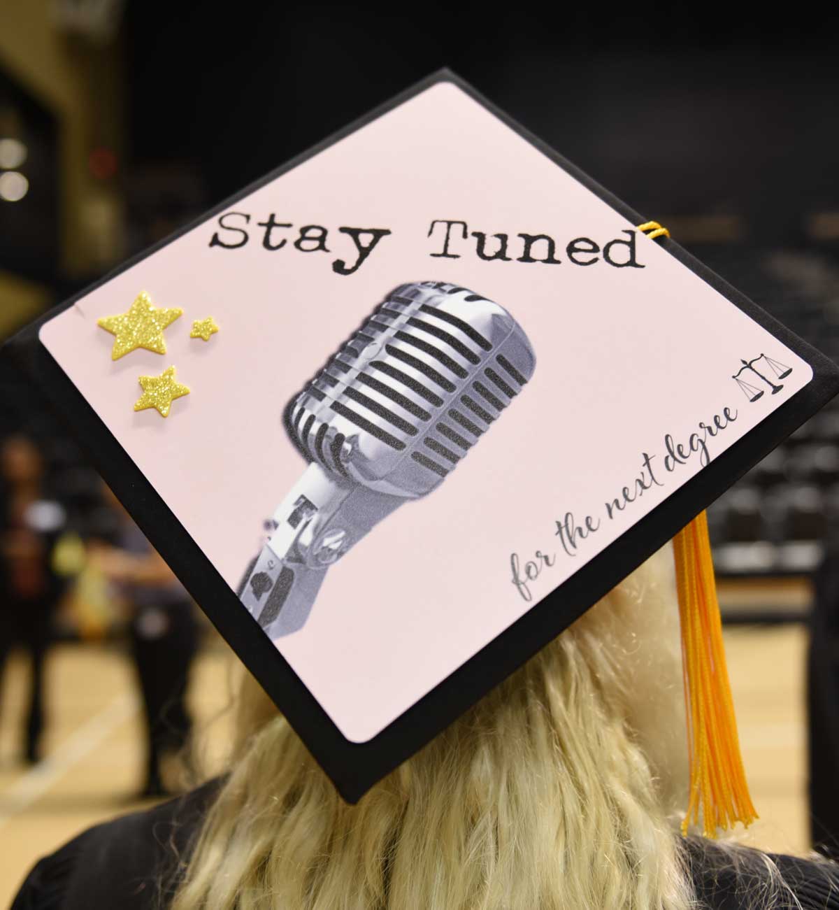 Grad cap decorated with microphone and text: Stay tuned
