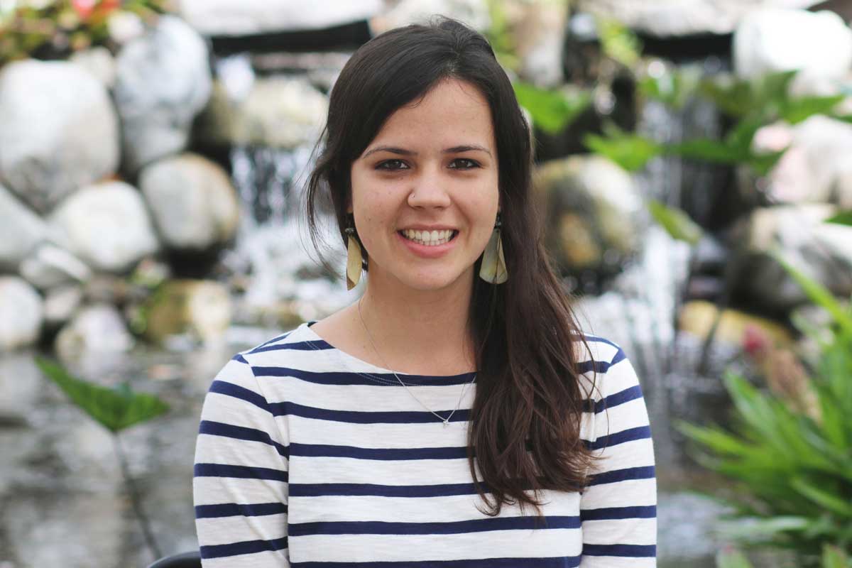 Brunette woman in white and blue stripe shirt stands in front of rocks