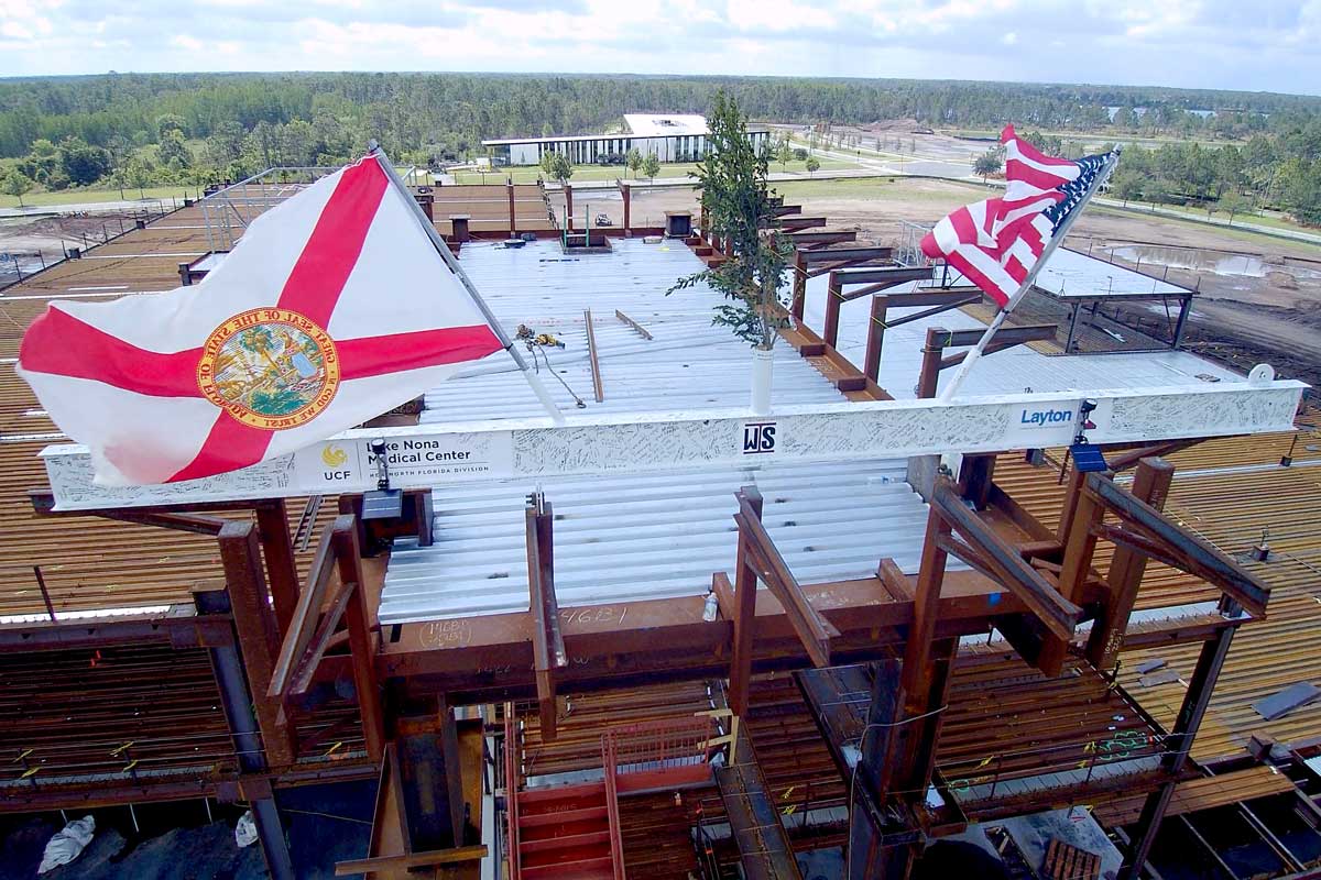 White beam sits atop construction framework with U.S. and State of Florida Flags waving atop the structure