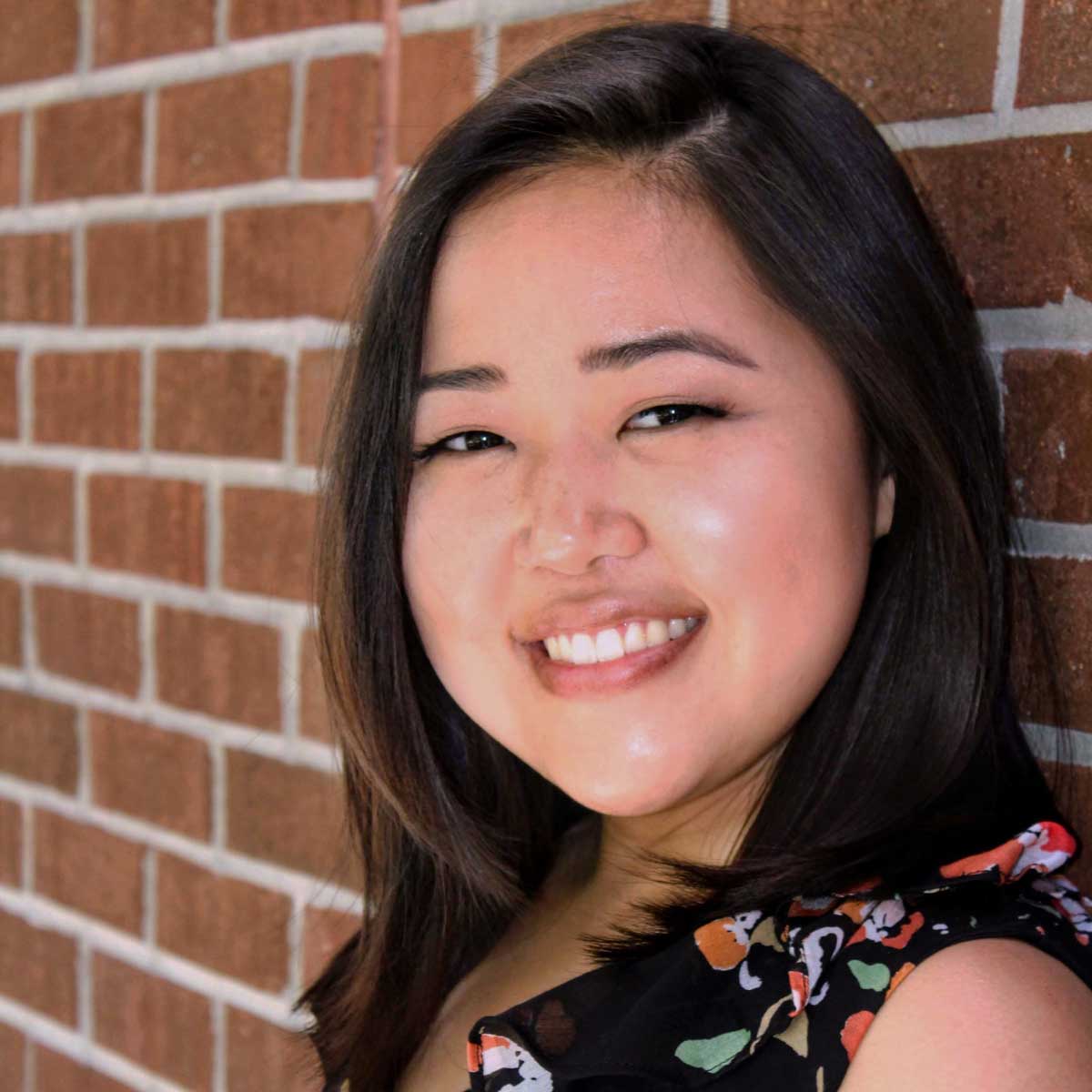 Asian woman dressed in a black blouse stands in front of brick wall