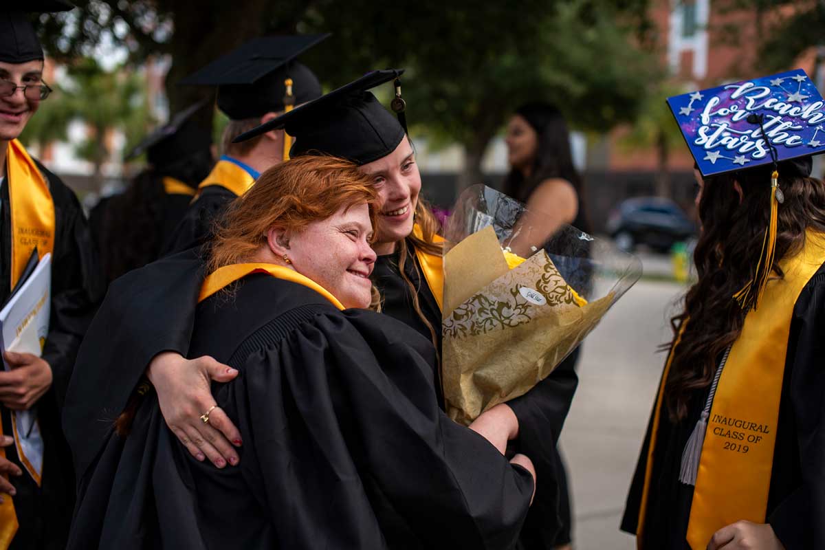 Two graduates in black caps and gowns side hug