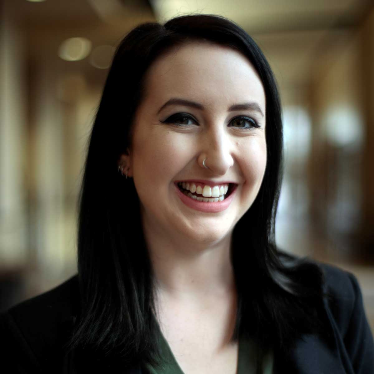 Brunette woman in black blazer stands in hallway