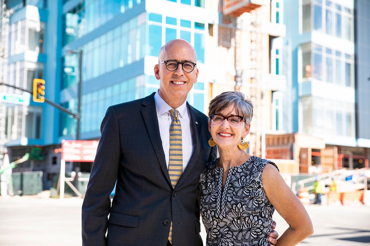 A man in a suite and a woman in a dress stand in front of buildings in downtown Orlando.