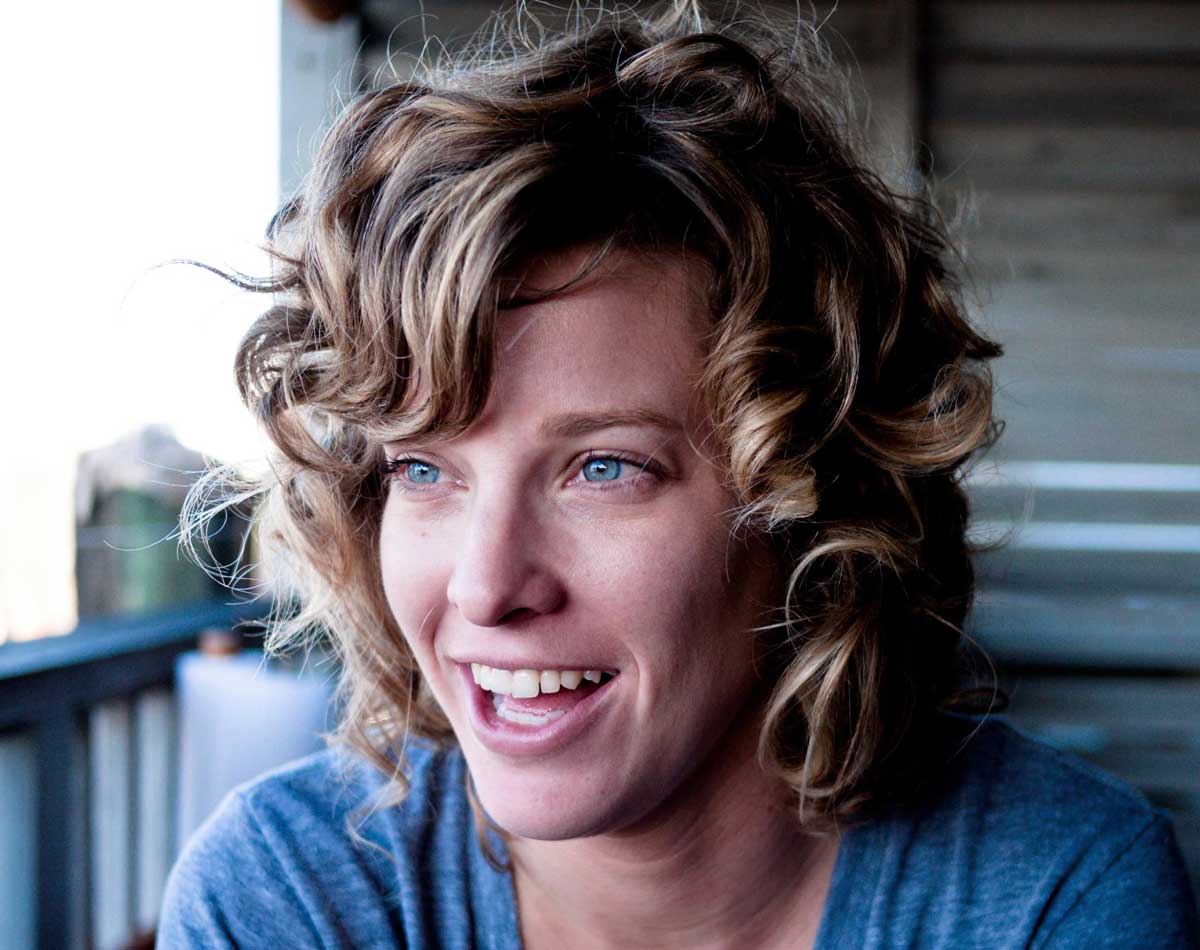 Blonde, curly haired woman in gray t shirt sits outside