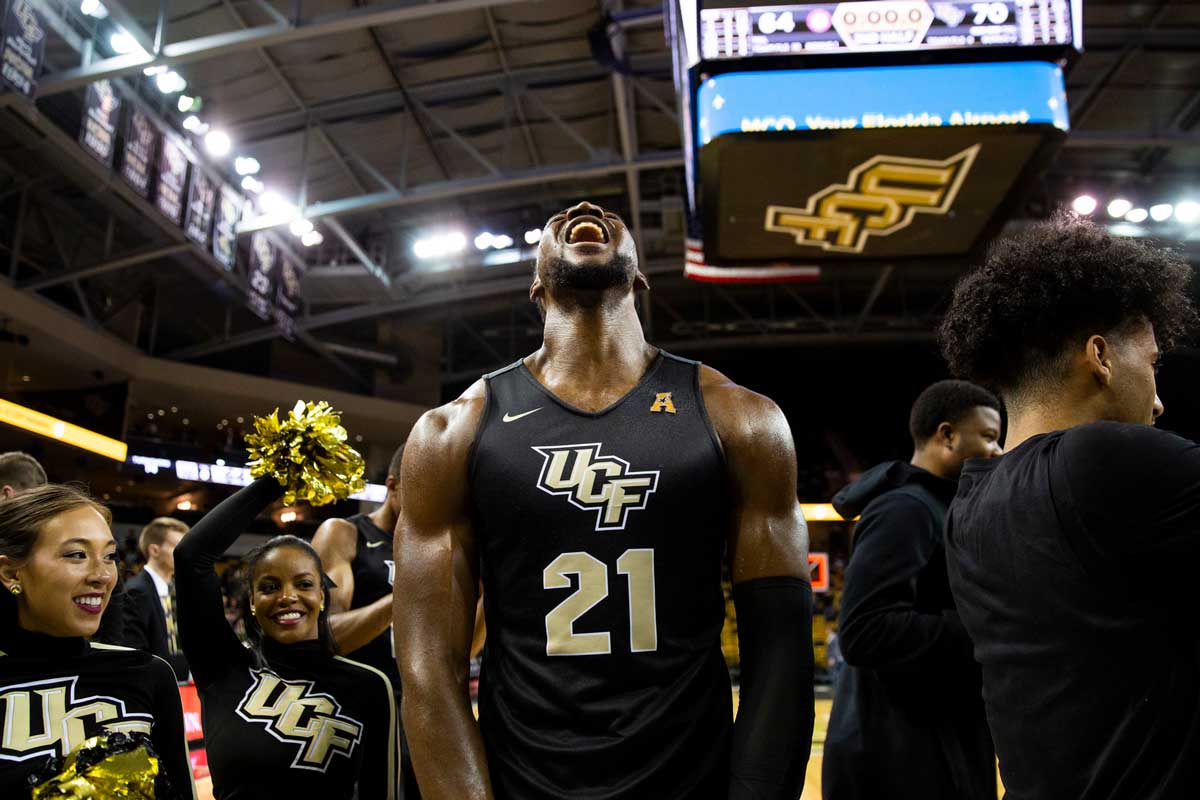 UCF basketball player Chad Brown flexes and yells with cheerleaders behind him