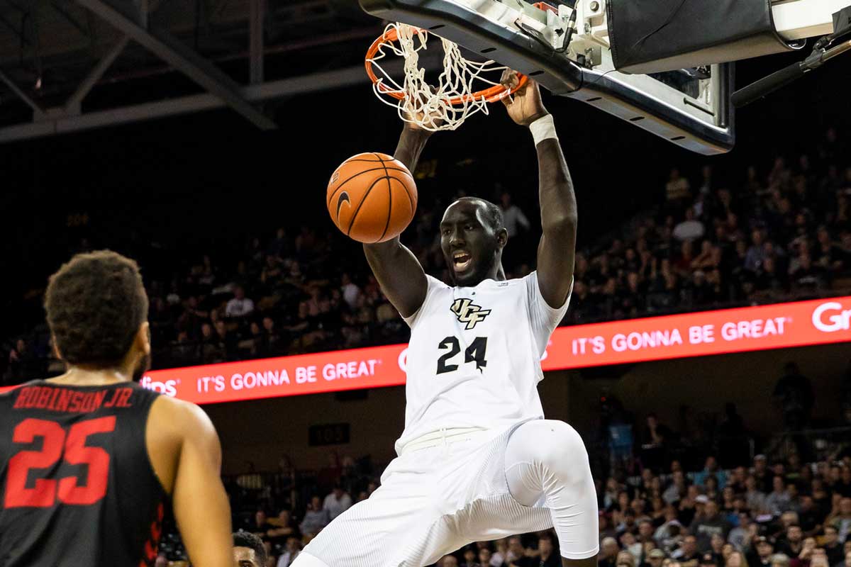 UCF basketball player Tacko Fall dunks while opponent looks on