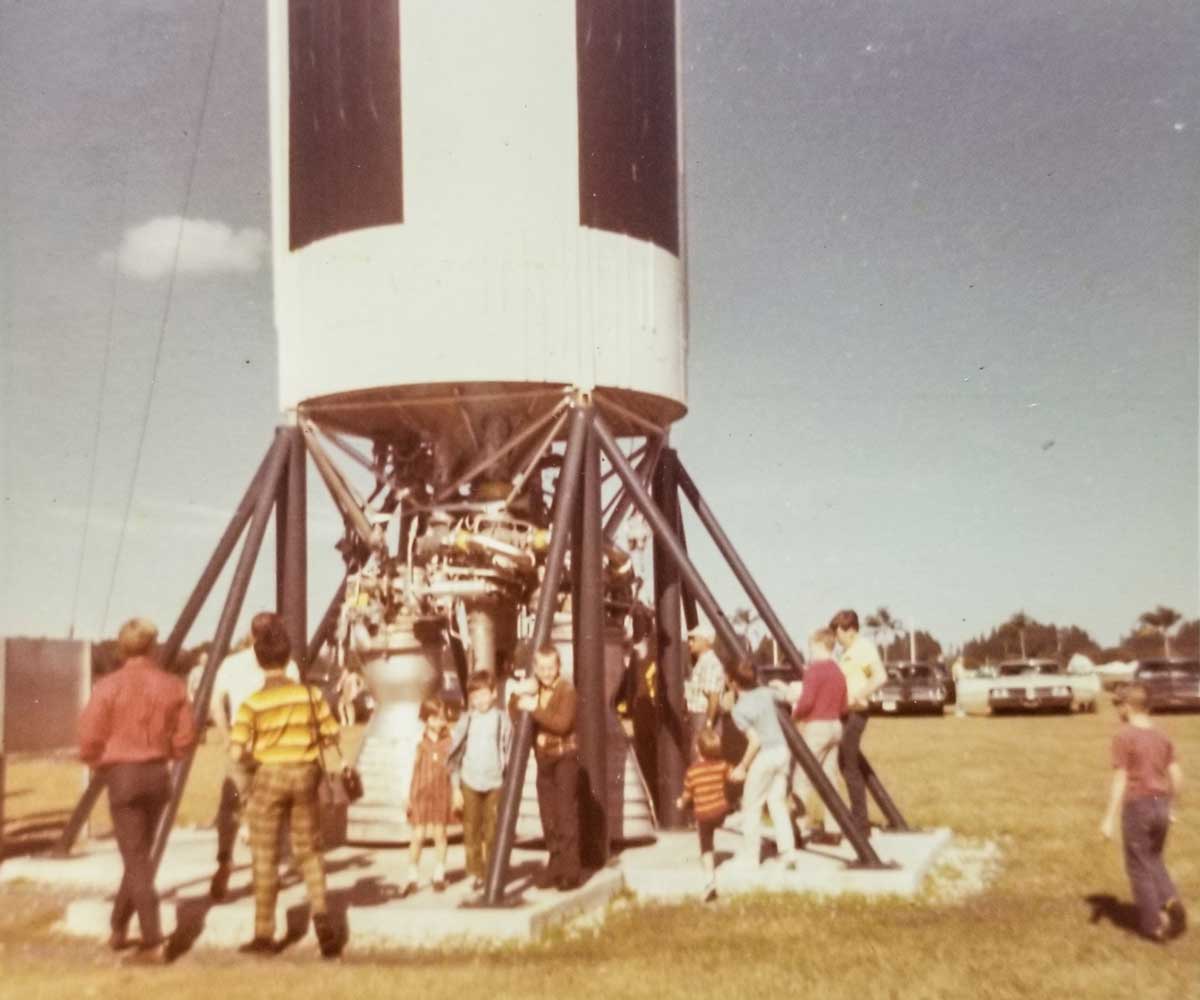 old photograph of the bottom of Apollo 11 and people walking around it on a sunny day