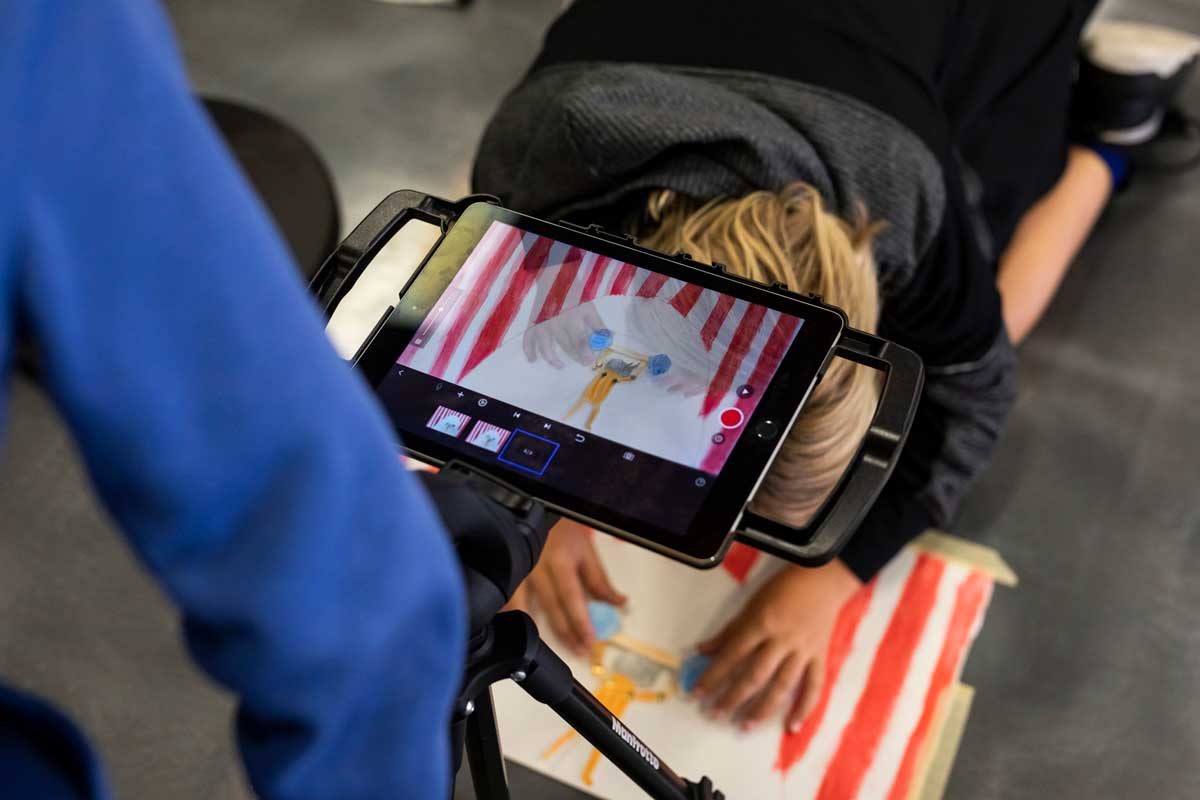 iPad screen focuses on drawing tapped to floor with a young boy moving the character in the drawing