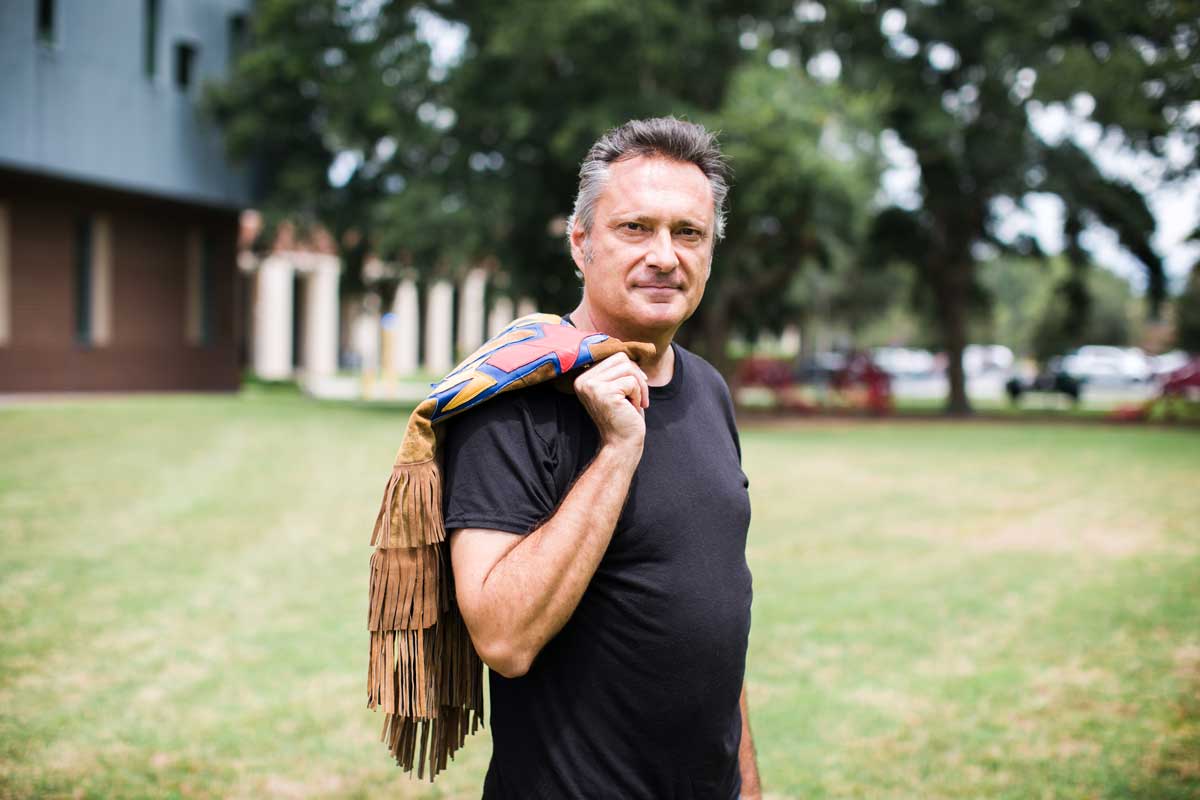 Man wearing black T shirt poses with fringe vest over his right shoulder