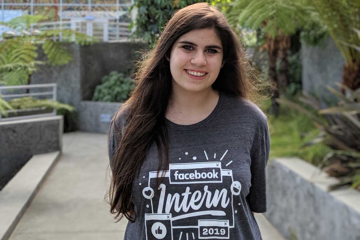 Female wearing Facebook Intern gray t shirt stands near shrubbery