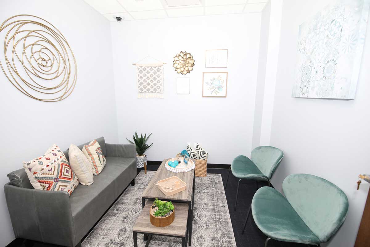 Soft interview room with a gray couch and pillows, coffee table and two green chairs