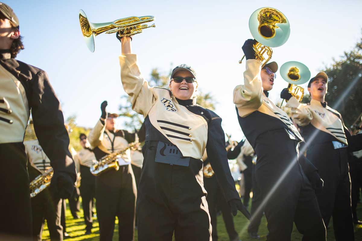 Members of UCF's marching band in black and gold uniforms hold up horns