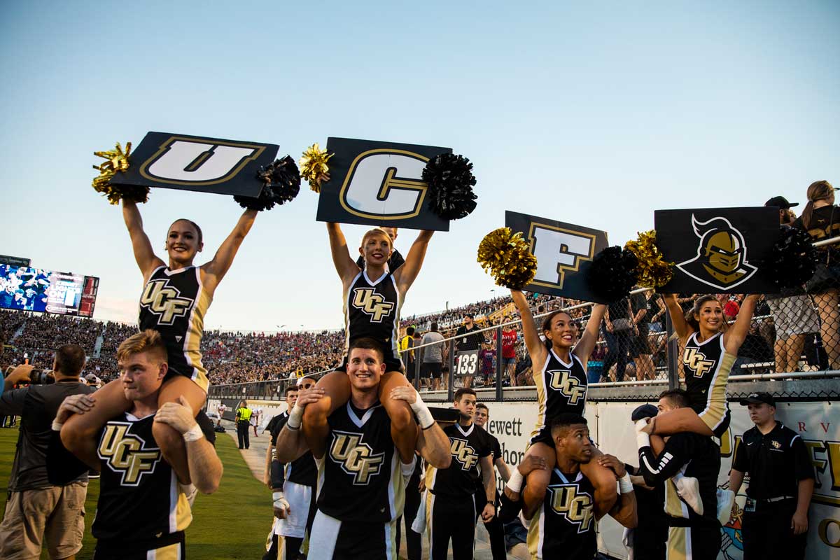 cheerleaders sit on shoulders of teammates and hold up U-C-F signs