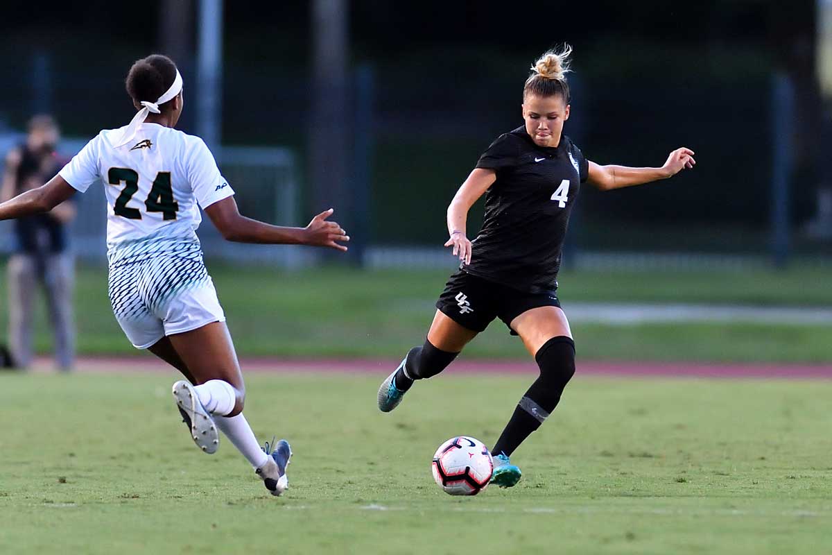 female soccer player wearing black uniform prepares to kick ball as opponent closes in