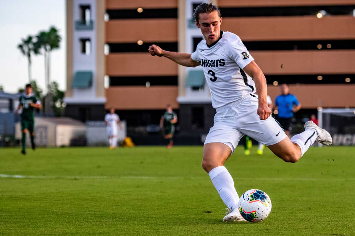 male soccer player wearing white jersey prepares to kick ball