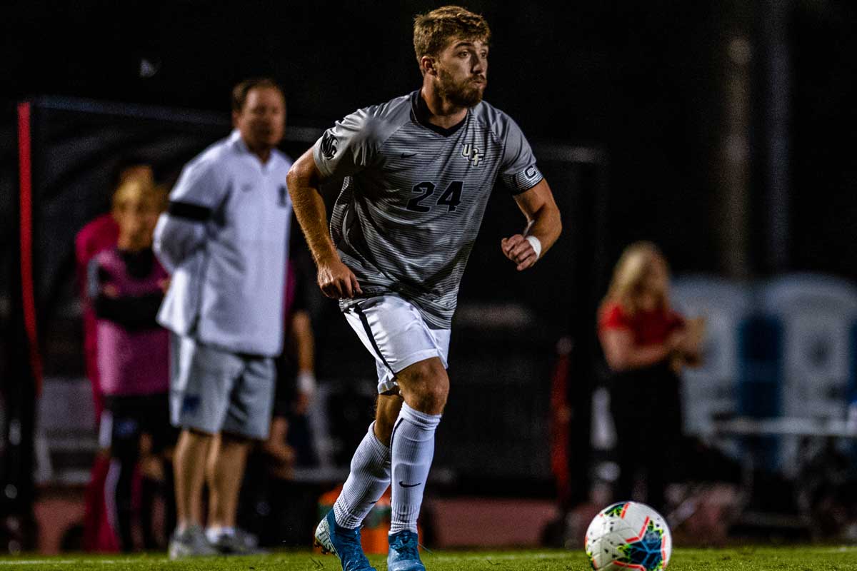 Soccer player wearing gray shirt and white shorts prepares to kick ball