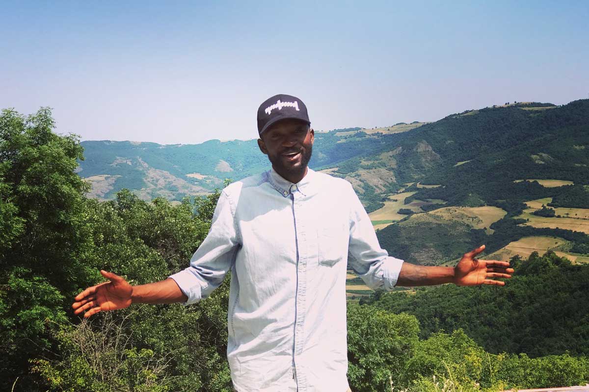 Man wearing baseball hat stands on a mountain top on a sunny day in Armenia.