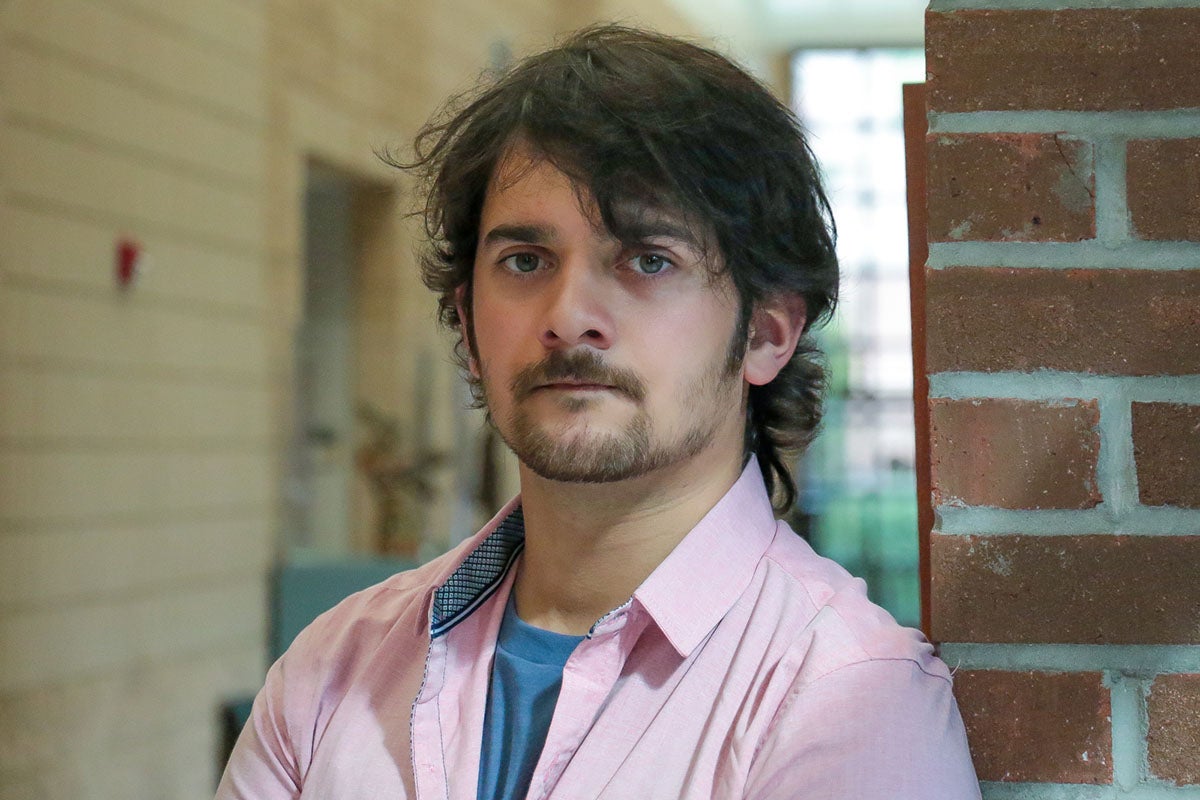 Portrait of brunette man wearing pink collar shirt stands near brick wall