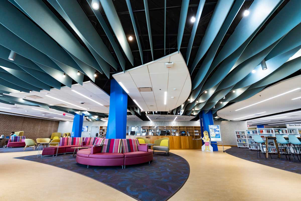 purple circular couches around blue poles in front of the circulation desk with white bookshelves off to the right