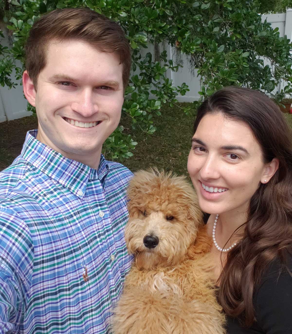 Man and woman hug a golden doodle dog