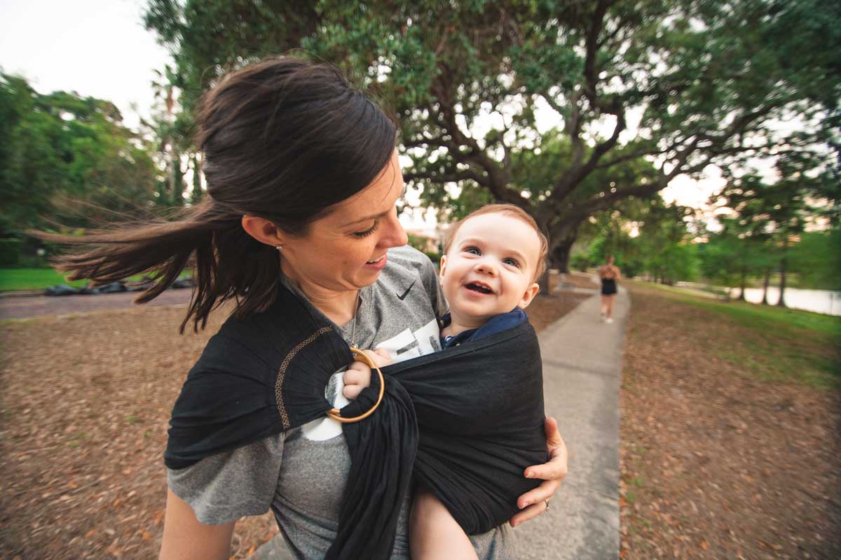 woman wears baby in black sling outside