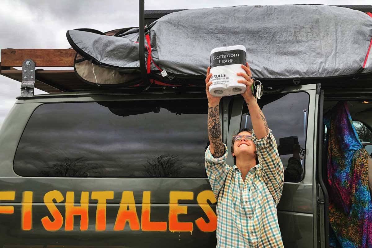 Megan Fish holds a package of toilet paper to the sky in front of her van