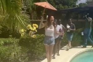 Woman holds umbrella dancing around pool on sunny day