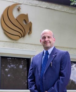 Portrait of Joe Thalheimer in front of Pegasus symbol on building