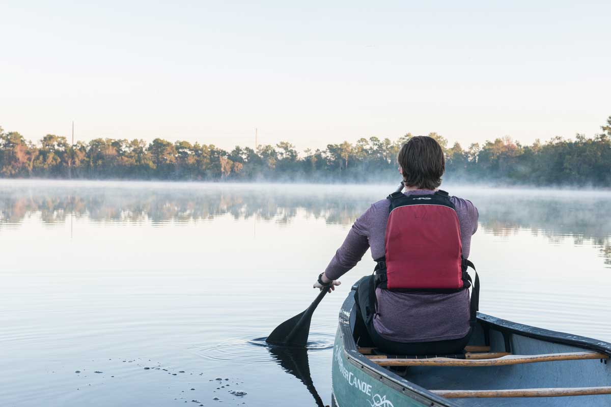 Man wearing life vest rows canoe on lake