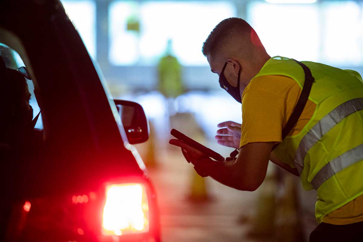 Man wearing yellow safety vest stands outside car to take information from passenger window