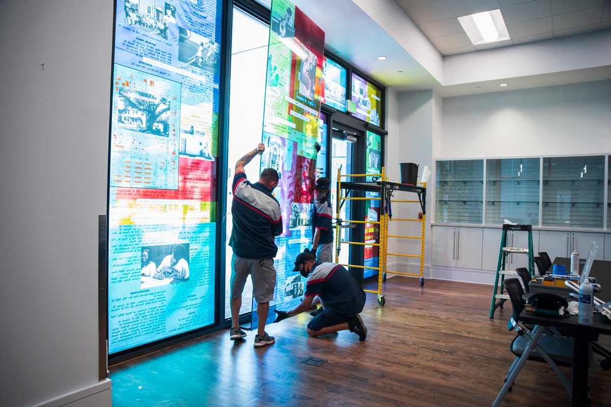 Three men install large glass panel into window frame